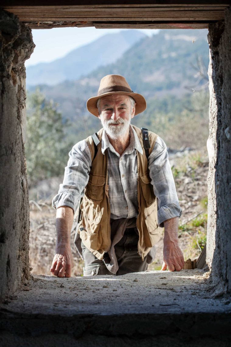 Man in hunting attire and hat looks in through a window from outdoors