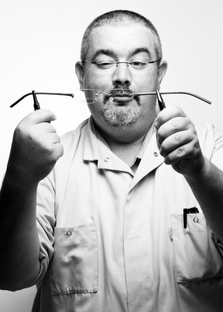Black and white photograph of a man wearing a lab coat, closely examining a pair of glasses