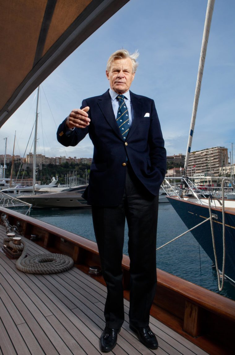 Man in suit standing on deck of a yacht in a harbour