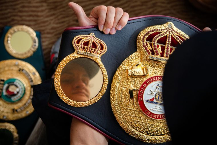 Close-up photo of a gold world champion boxing belt with a man&#039;s reflection visible in the belt