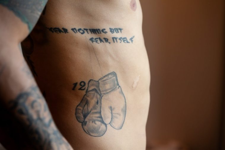 Close-up photograph of a man's torso in profile with tattoos of text and boxing gloves
