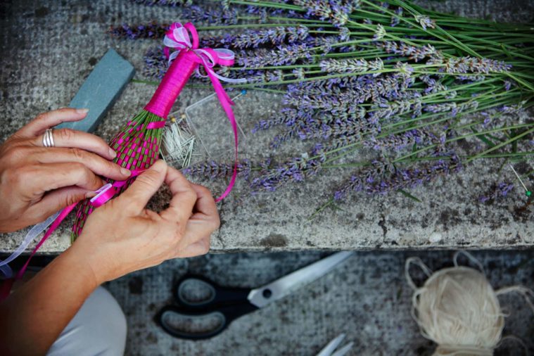 Close-up photograph of hands working with stalks of lavender to make a craft item