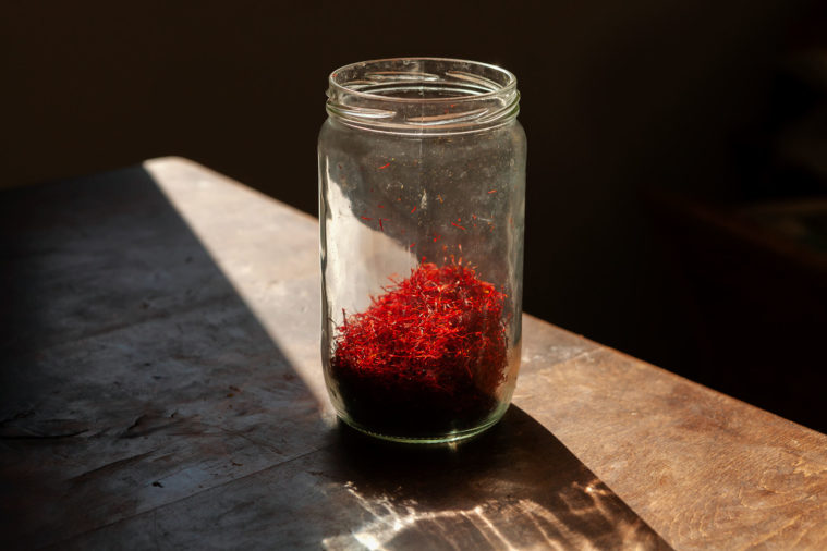 Close-up photo of a jar full of red saffron stamens in a ray of sunshine