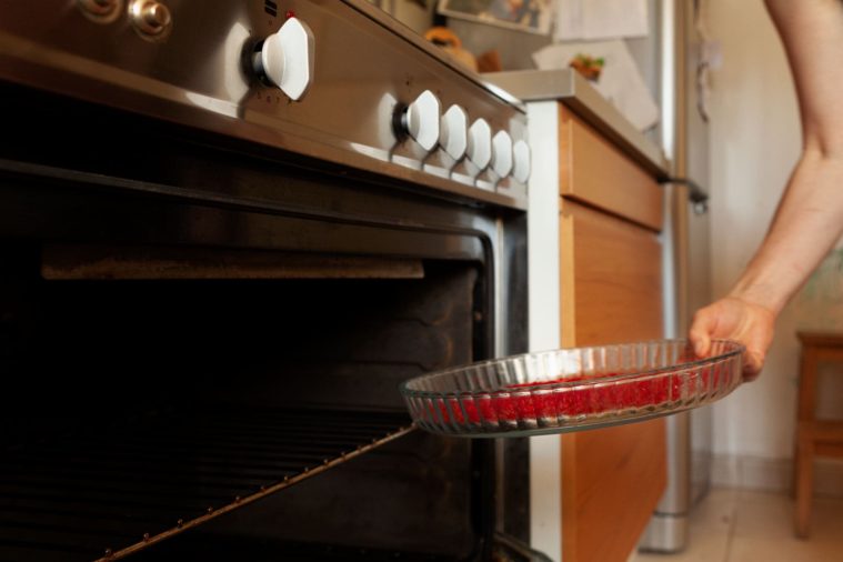 Close-up photo of a hand putting a dish full of red saffron stamens into an oven