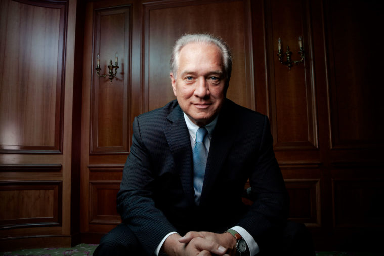 Man in suit poses for a photograph, seated in wood-panelled room