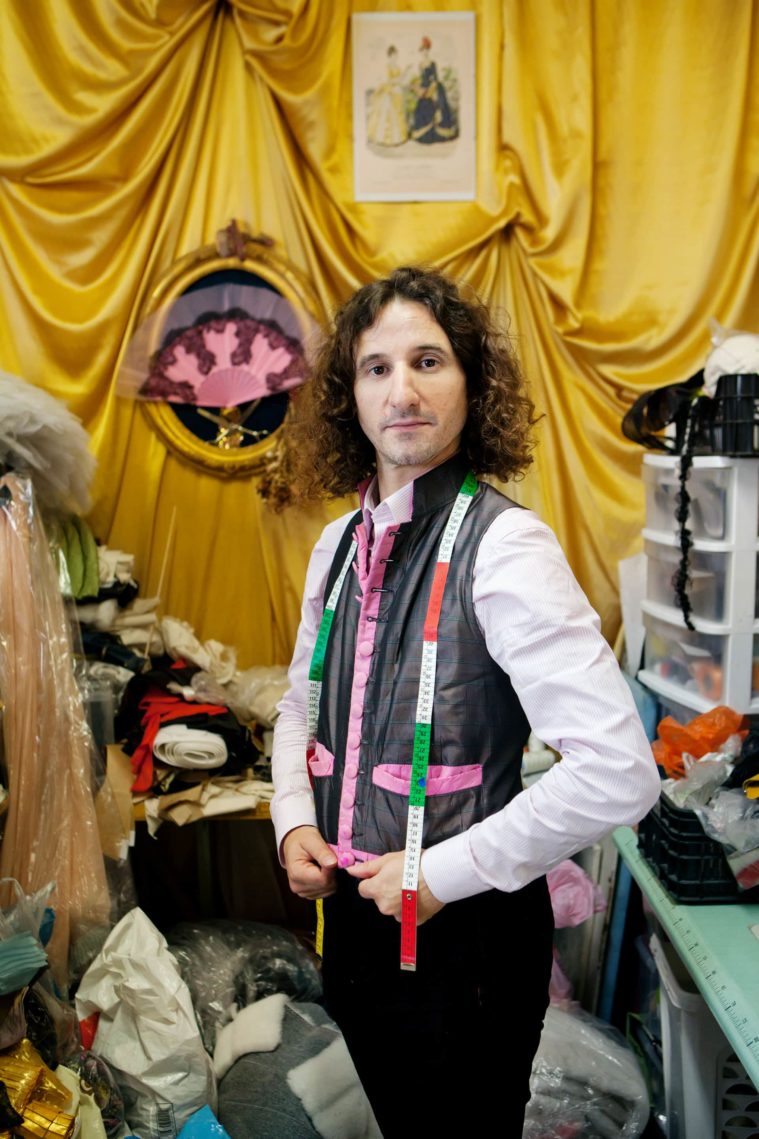 A tailor with measuring tape around his neck poses for a photograph in his workshop