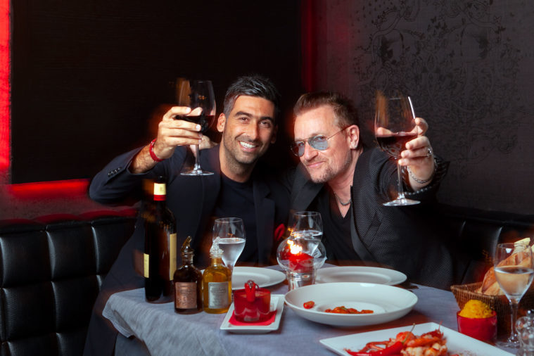 Two men sitting in a restaurant raise wine glasses to the camera