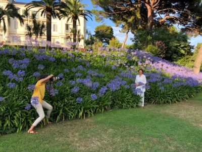 Photographer in yellow shirt points long lens at a woman in a garden of blue flowers