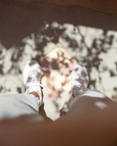 Photograph of the photographers feet in white trainers under the shadow of a tree