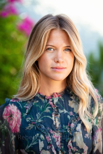 Portrait of a young blonde woman wearing a patterned floral dress, out-of-focus flowers in the background