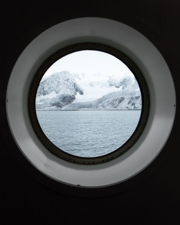Photograph of snowy ,coastal cliffs taken through the porthole of a ship
