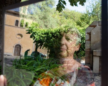 Photograph of the reflection of a woman in a sheet of glass that she holds in front of a chapel