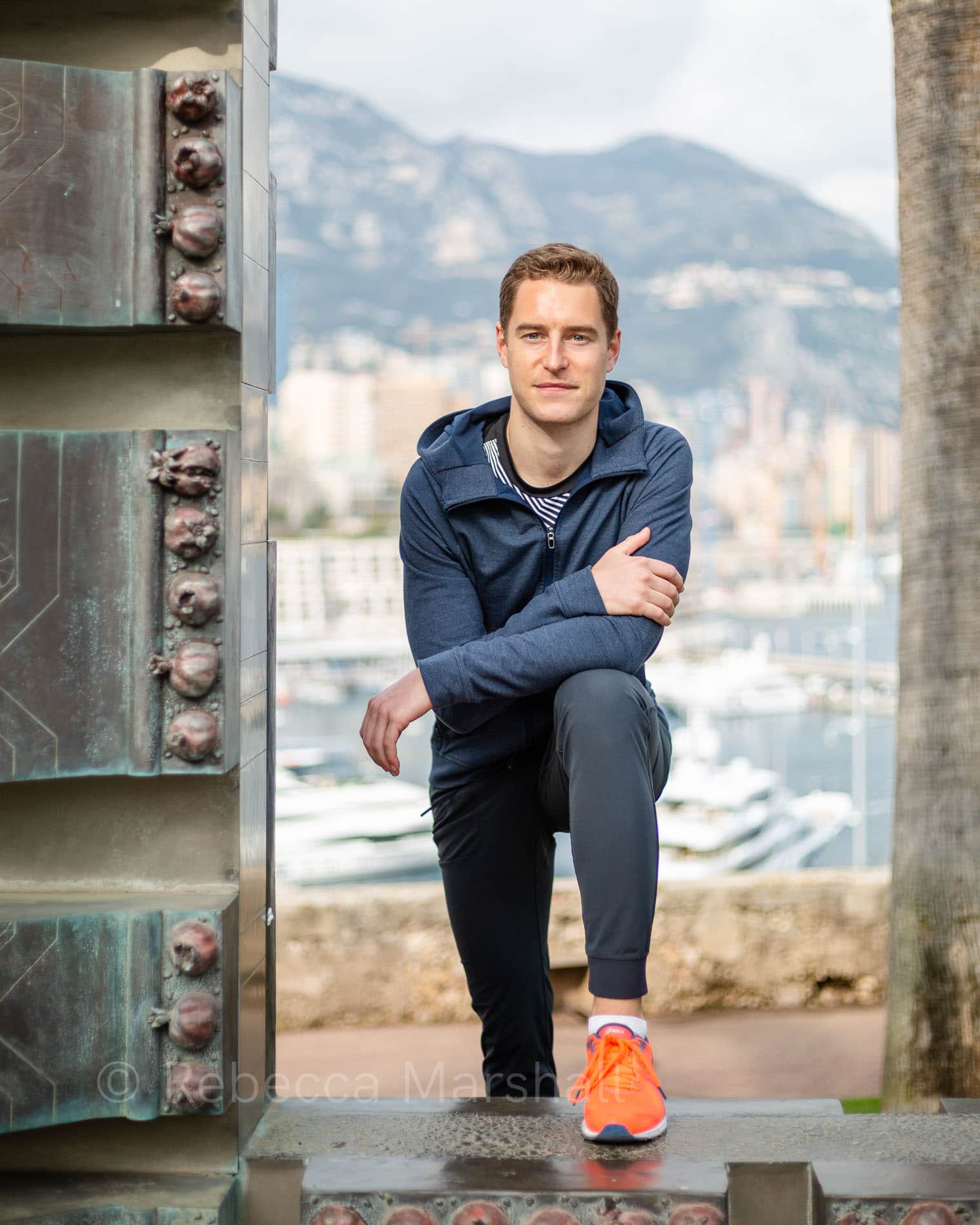 Portrait of man in sportswear standing on a monument overlooking Monaco harbour