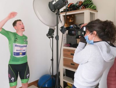 Photographer at work making a portrait of a cyclist with a studio flash in front of a white wall
