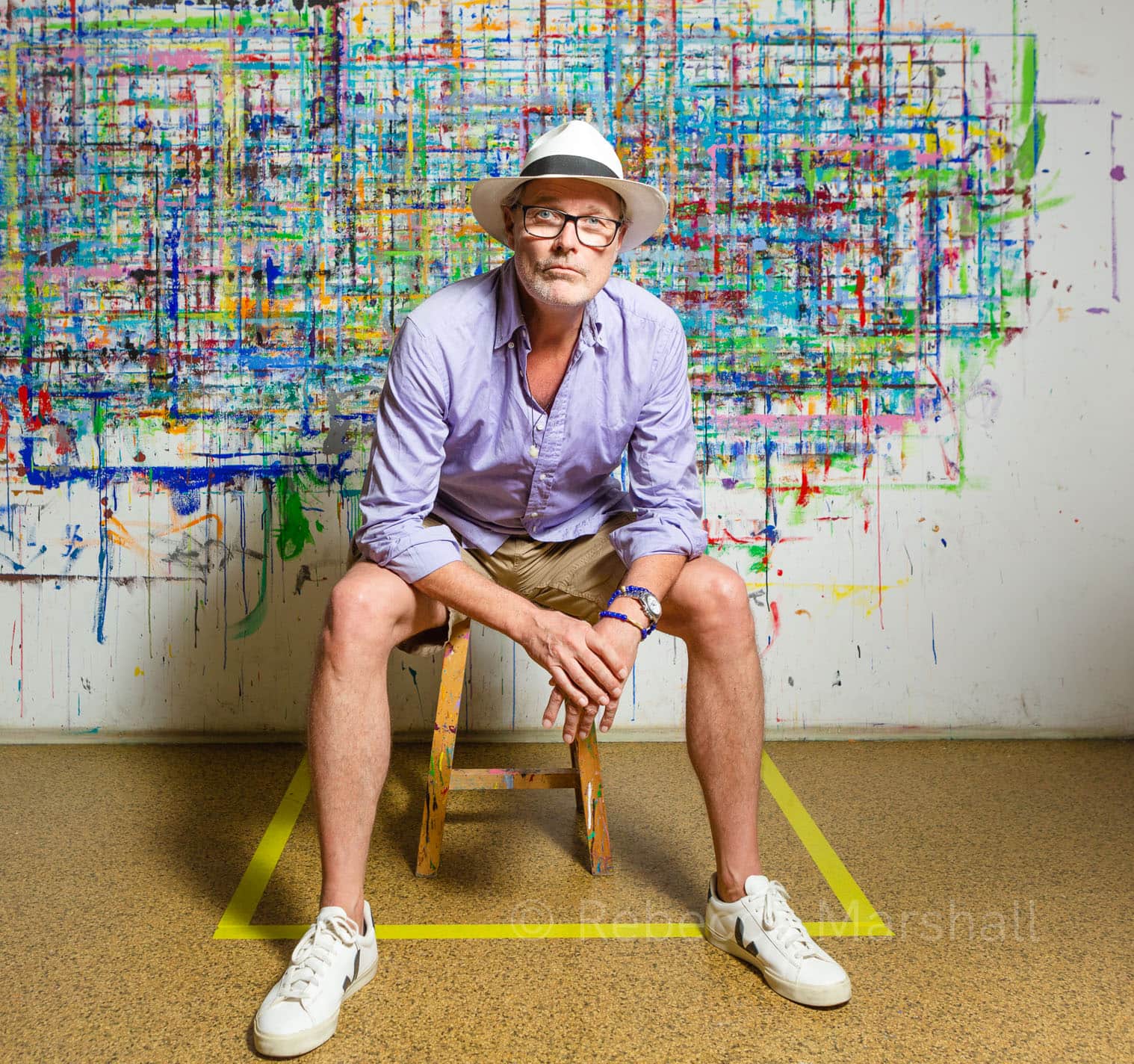 Portrait of a man wearing a white hat and sitting in front of a modern artwork
