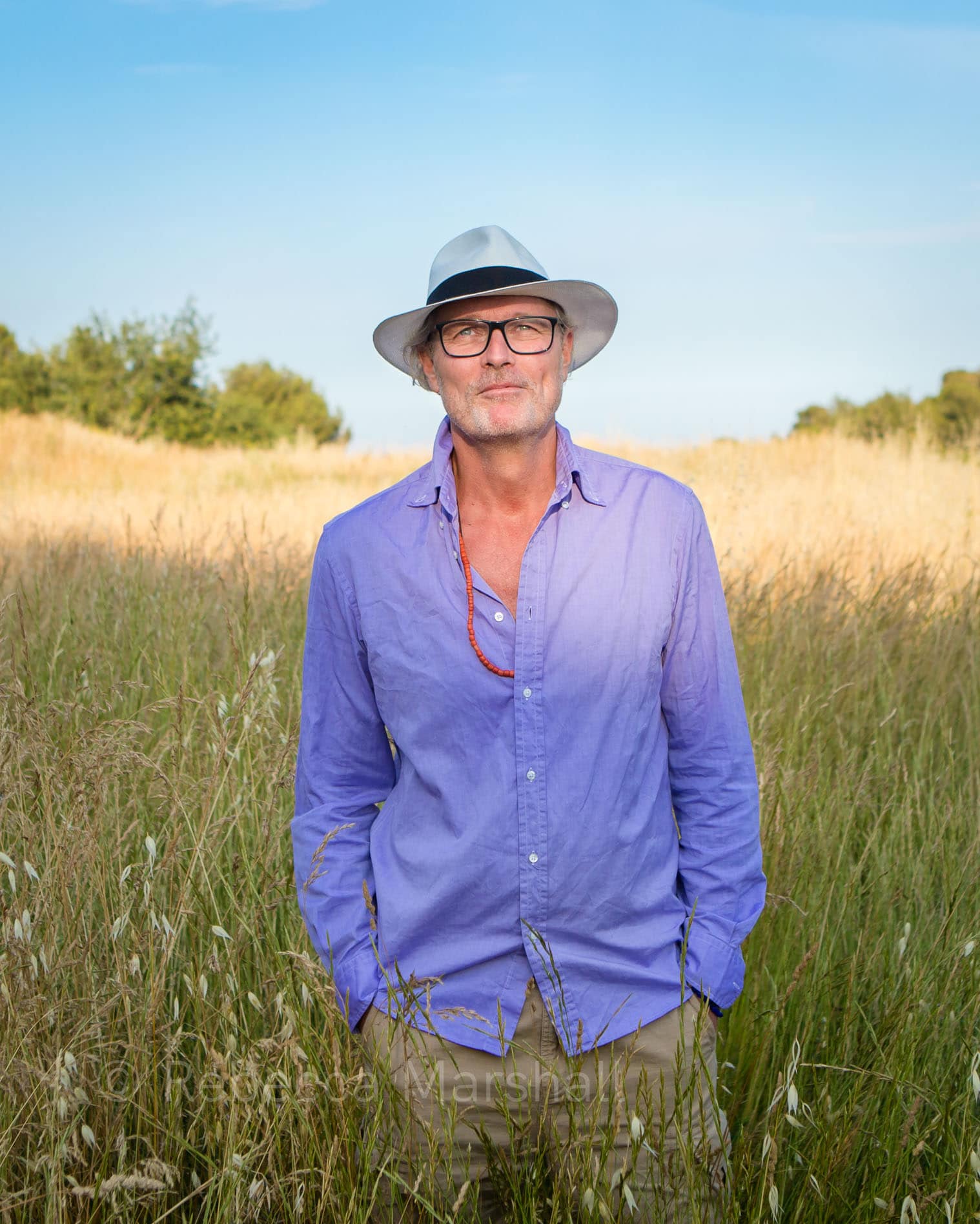 Photographic portrait of a man standing in a cornfield in a white hat and purple shirt