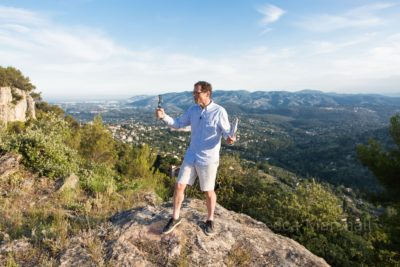 Photo of a man standing on a rock at the top of a hill making a video of himself