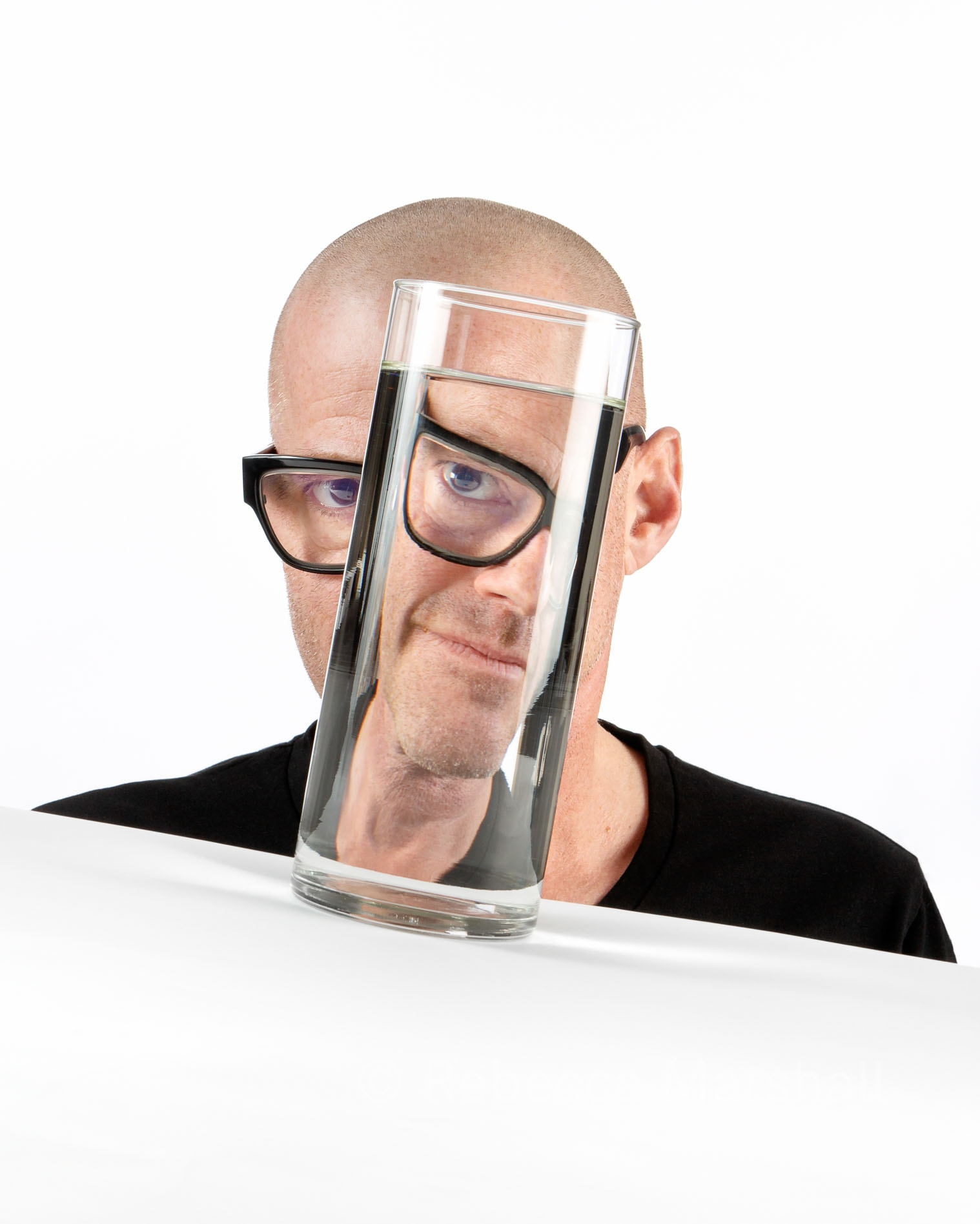 High key studio portrait of chef Heston Blumenthal looking through a glass of water on a slant