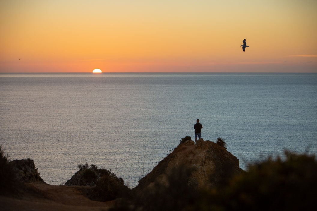 Photograph of the silhouette of a man standing on a dune watching the sunrise