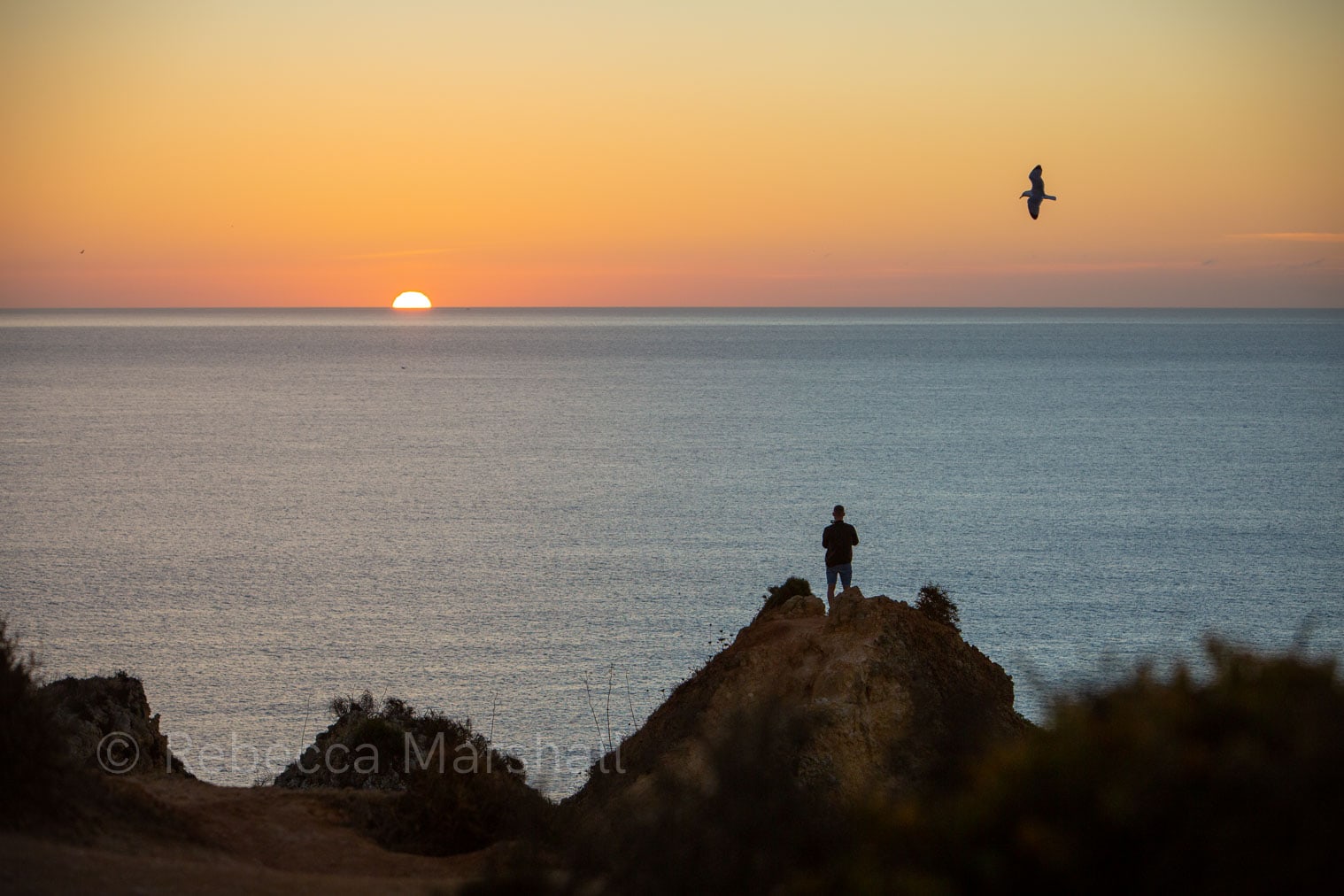 Photograph of the silhouette of a man standing on a dune watching the sunrise