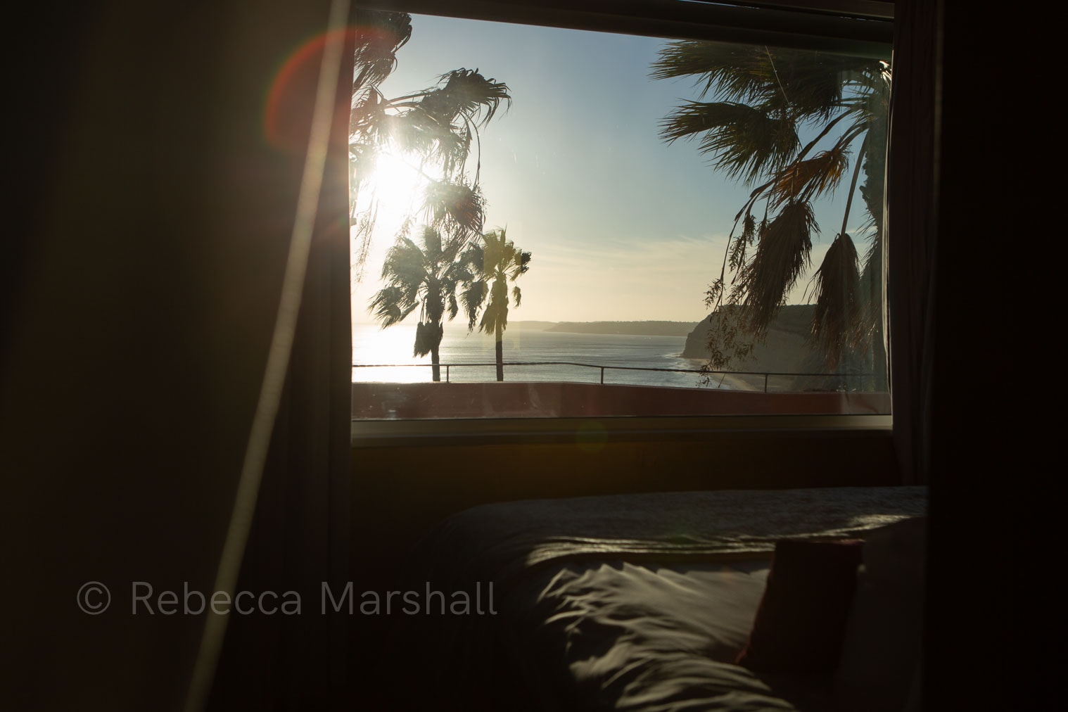 Photograph through a bedroom window of palm trees and a coastline