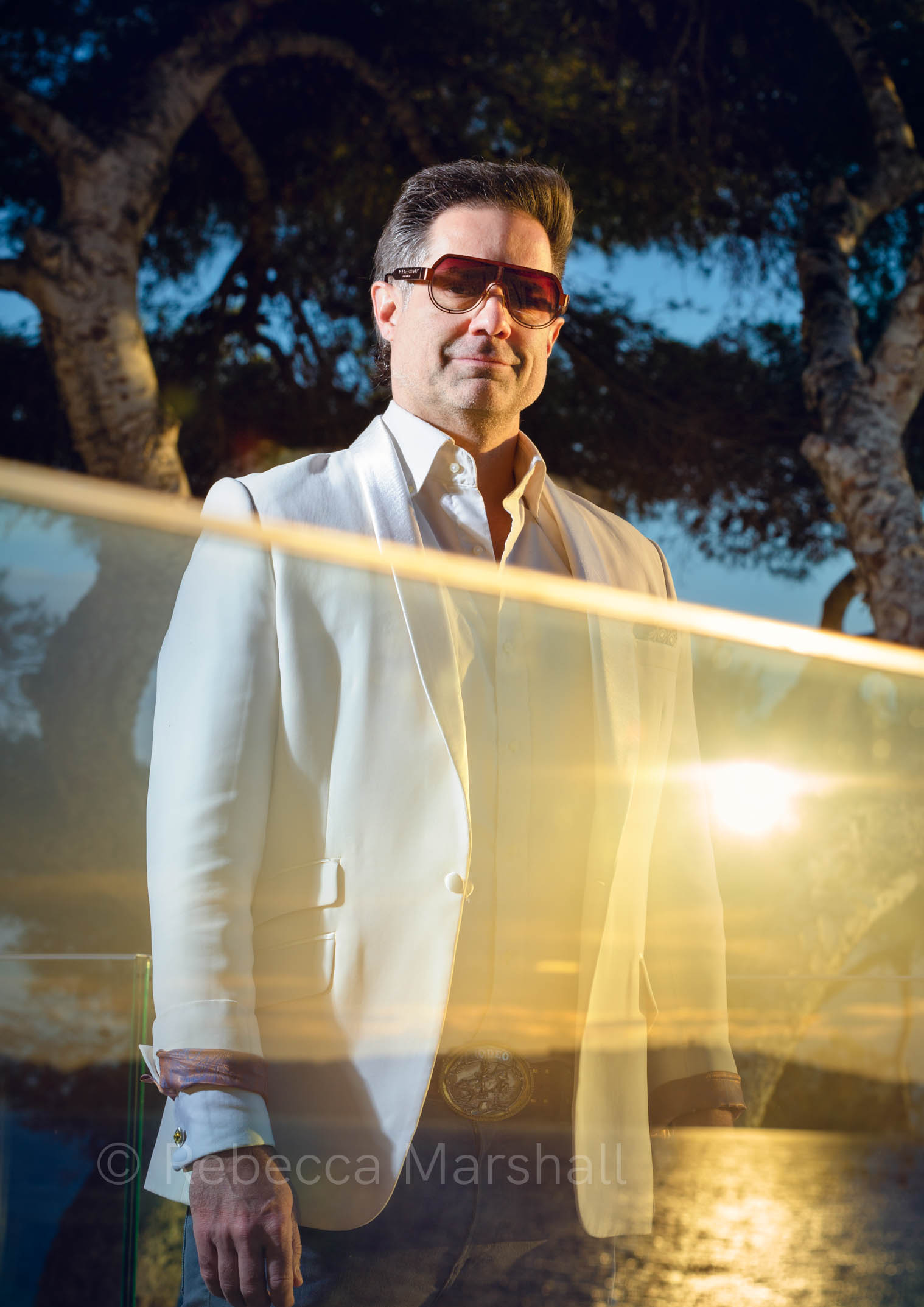 Portrait of a man in sunglasses standing behind a glass wall reflecting the sunset