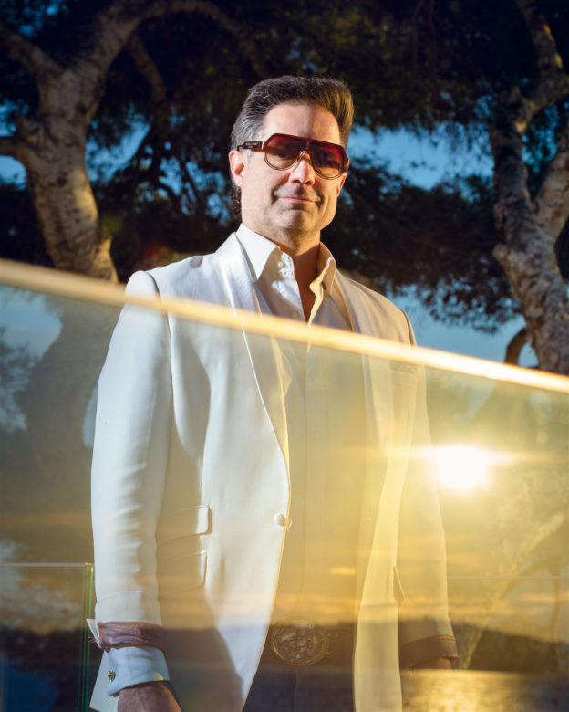 Portrait of a man in sunglasses standing behind a glass wall reflecting the sunset