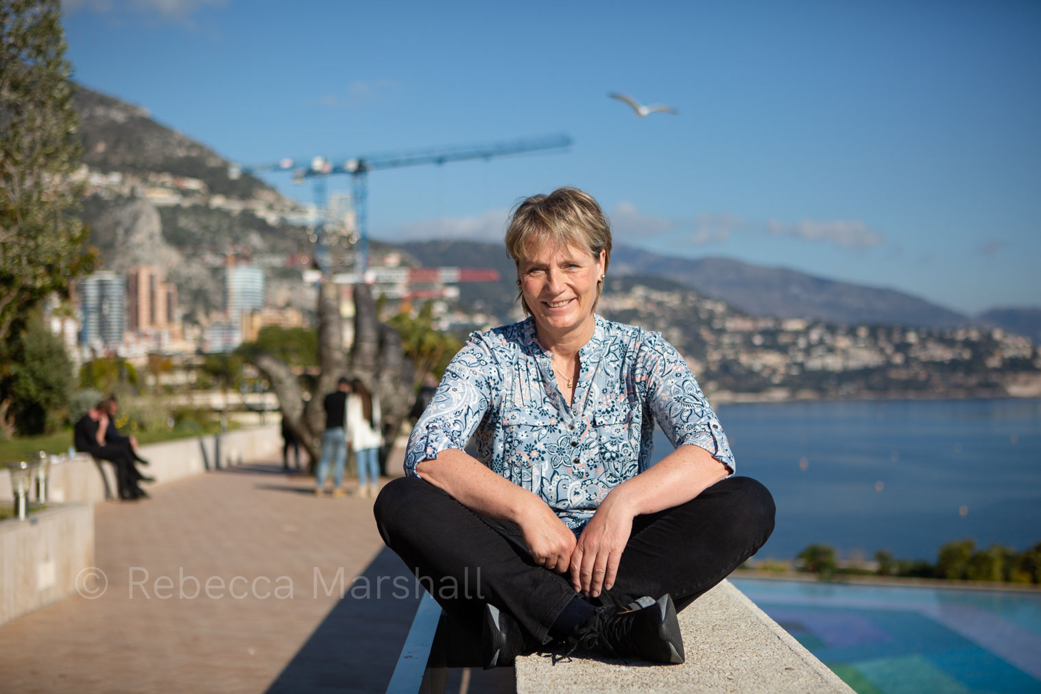 Woman sitting on a wall with the sea and blue sky in the background