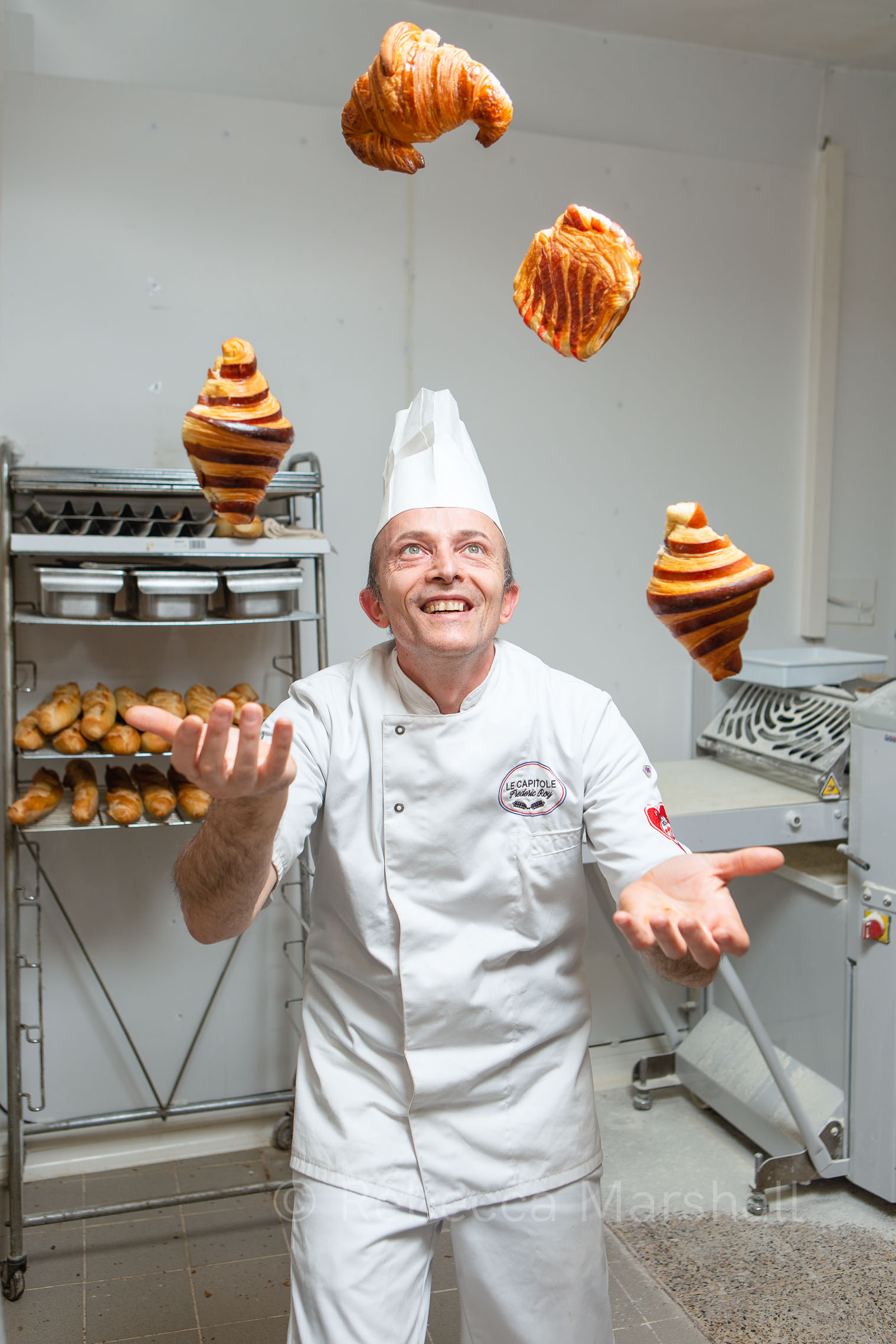 Portrait of a smiling baker juggling 4 croissants