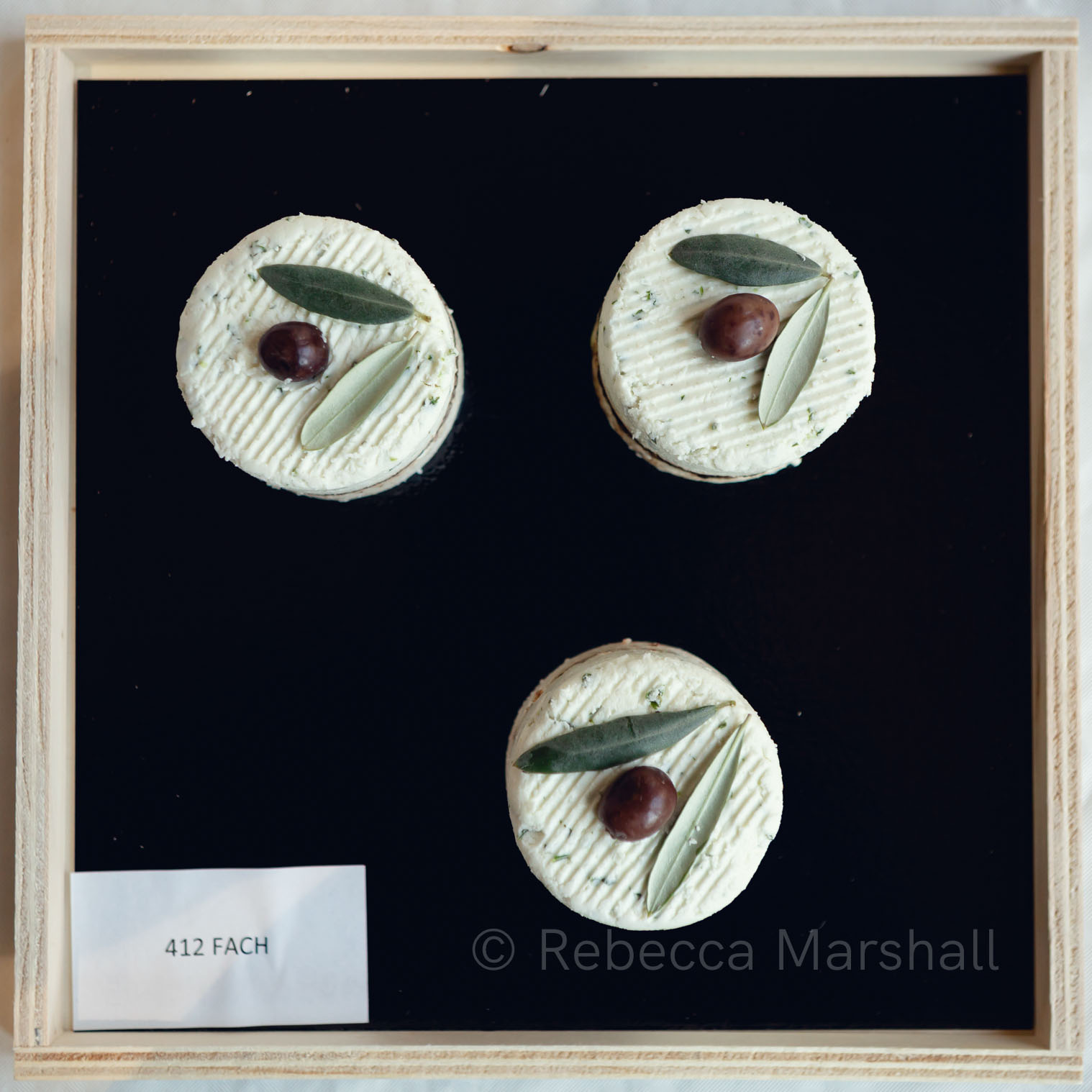 Photograph of 3 round cheeses with olives on top