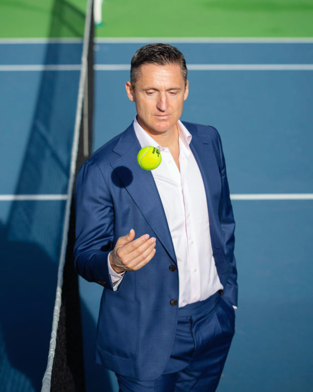 Photograph of Andrea Gaudenzi in a suit throwing a tennis ball on a tennis court