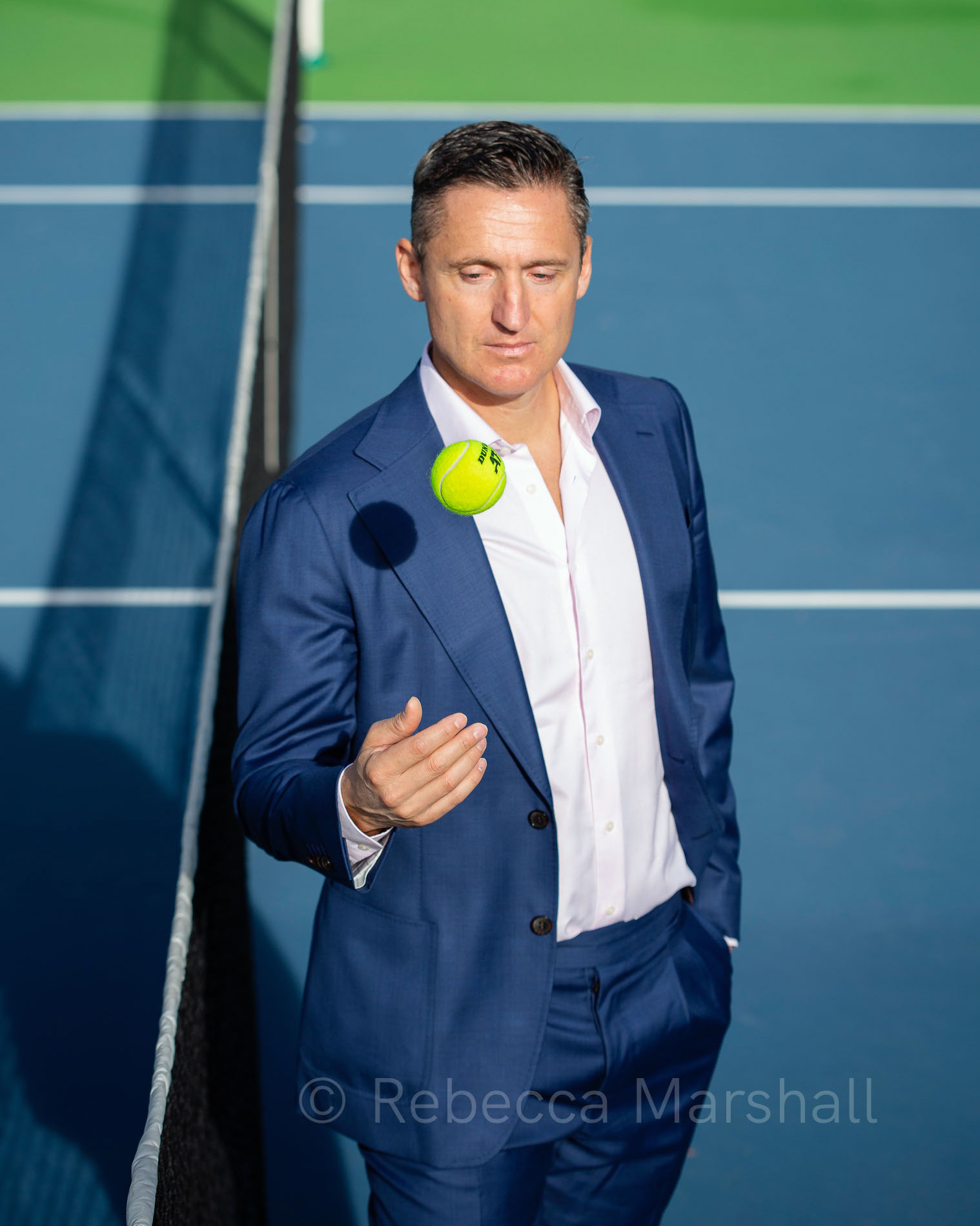 Photograph of Andrea Gaudenzi in a suit throwing a tennis ball on a tennis court