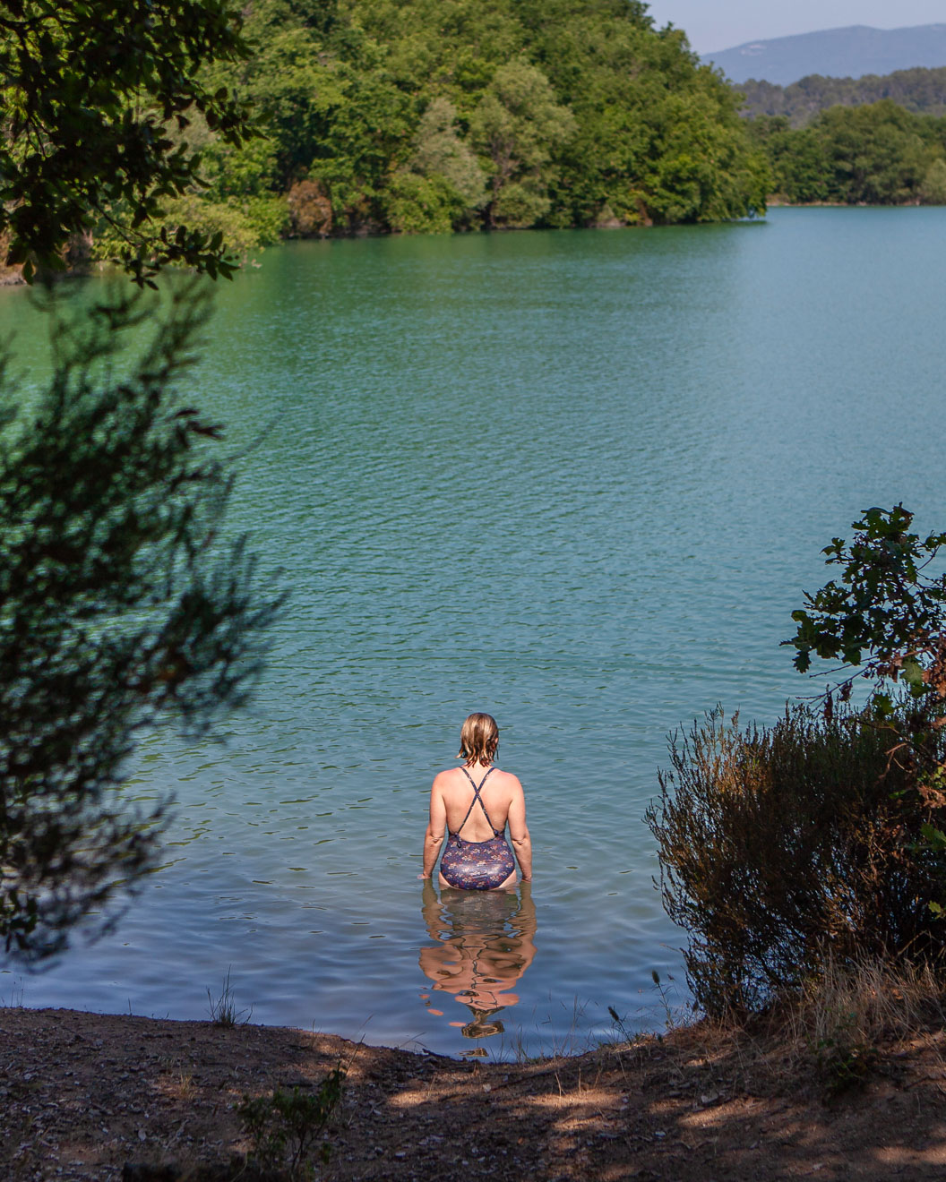 Photograph of a blond woman in a swimsuit entering an empty lake