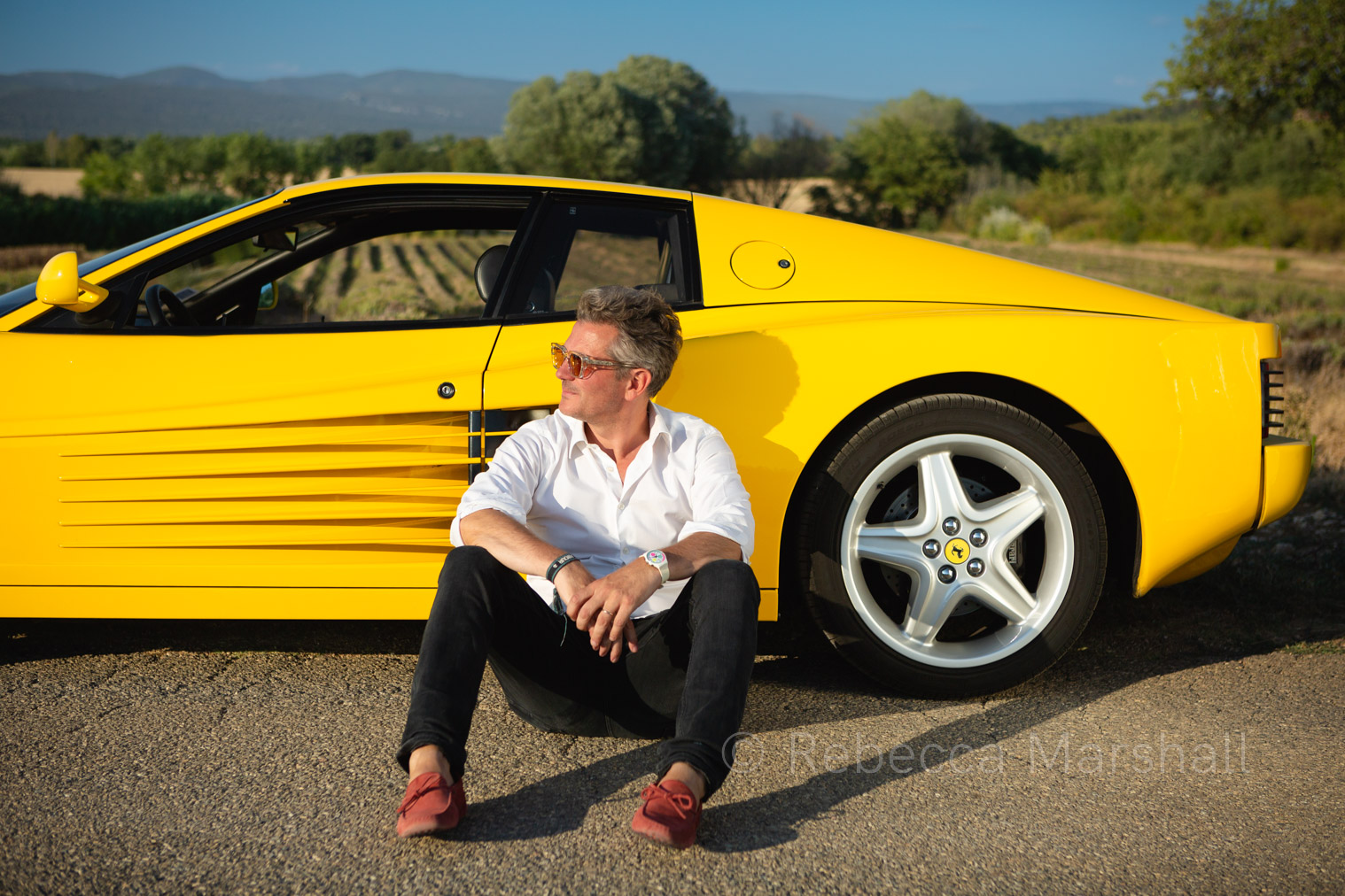 Man in white shirt poses for the photographer sitting in front of his yellow Ferrari