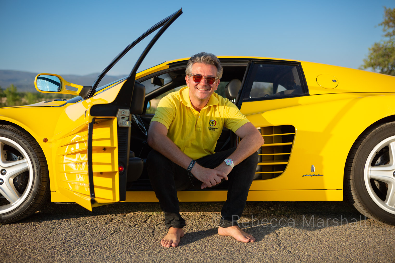 Man in white shirt poses for the photographer sitting in his yellow Ferrari
