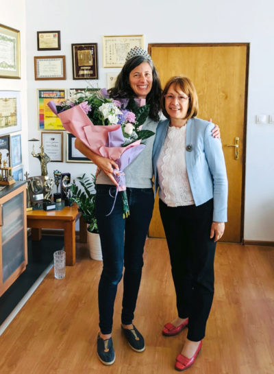 Photo of Rebecca Marshall posing with the mayor of Kazanlak, Bulgaria, wearing a crown and holding a bouquet of flowers