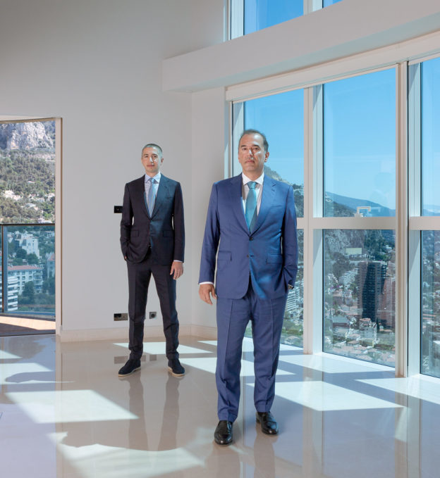Portrait of two men in suits standing by windows in a modern duplex apartment