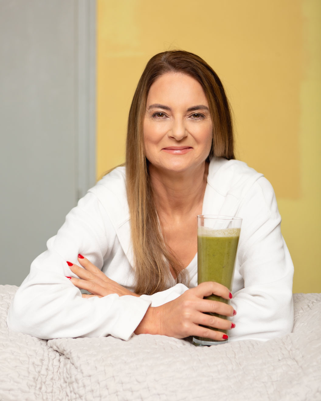 Photograph of a woman smiling in a white bath robe holding a green smoothie