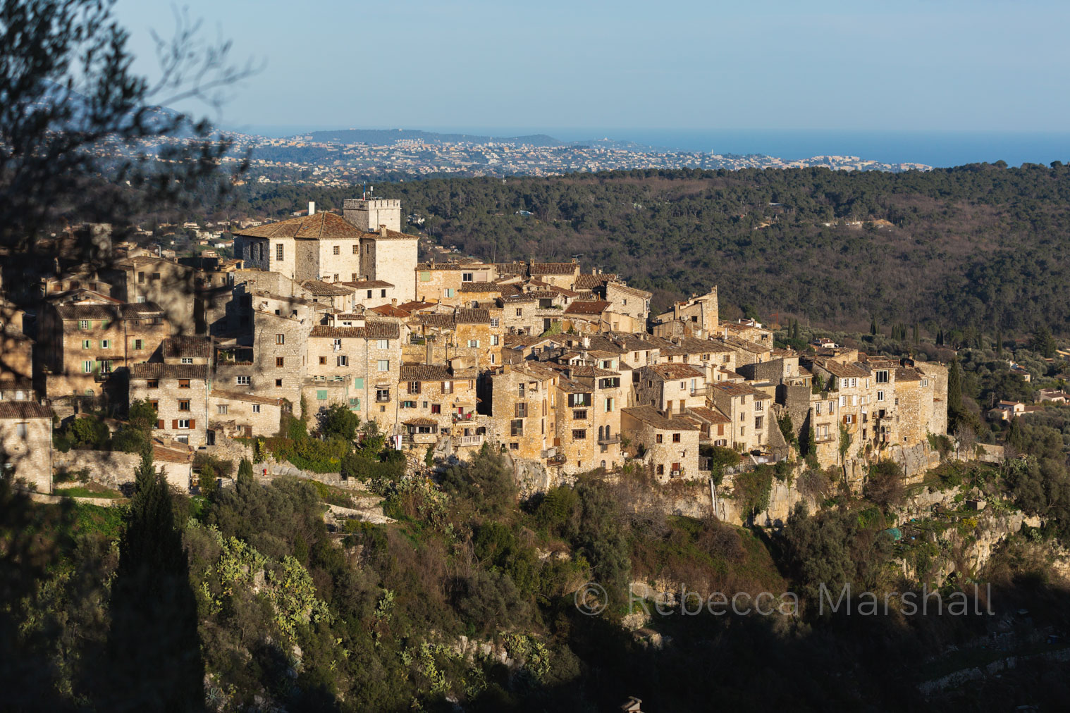 Photograph of medieval hilltop village with blue sky and sea in the background