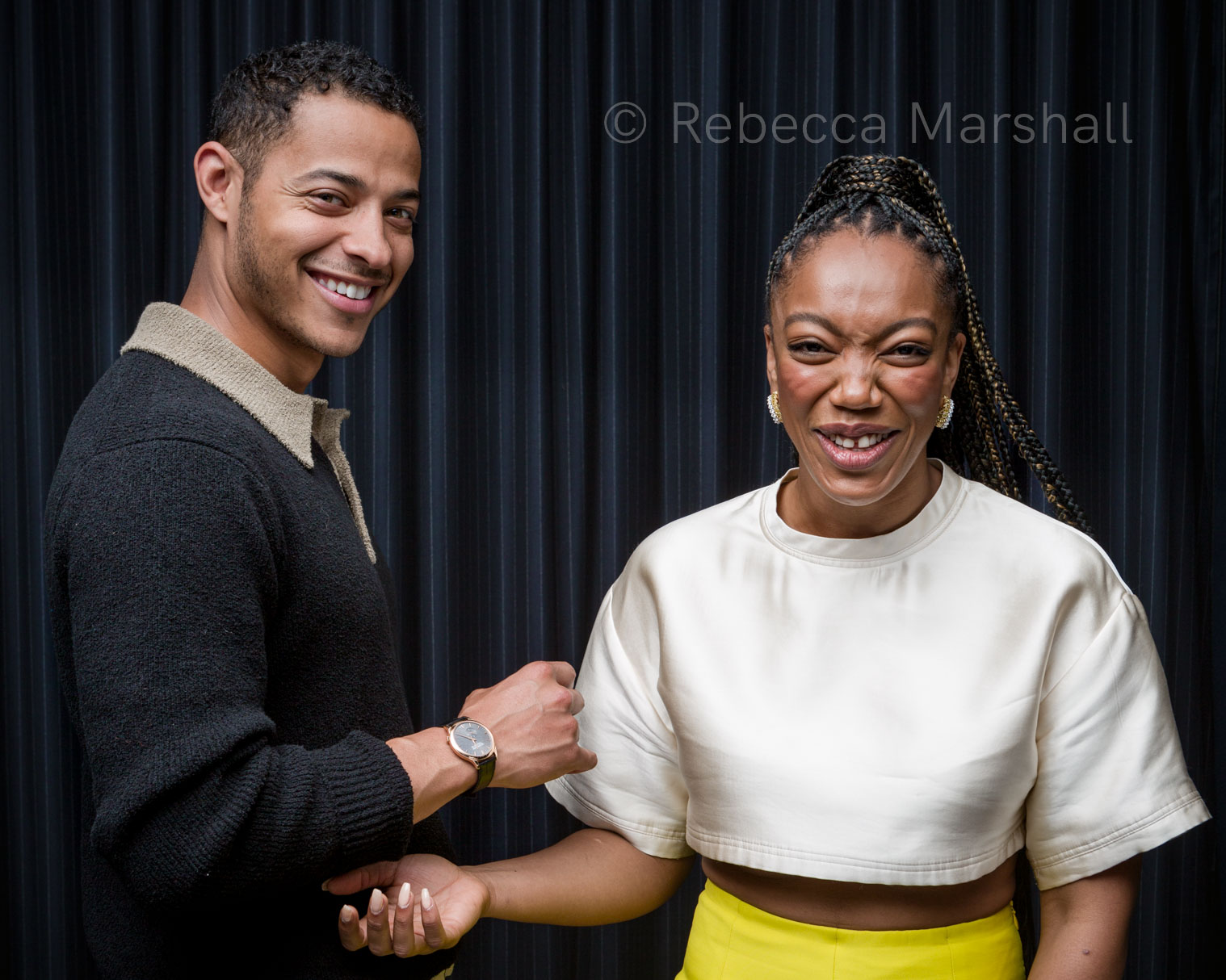Actors Daryl McCormack and Naomi Ackie laughing in front of a black curtain