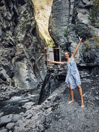 Woman in swimsuit smiles at camera at the foot of a grey cliff