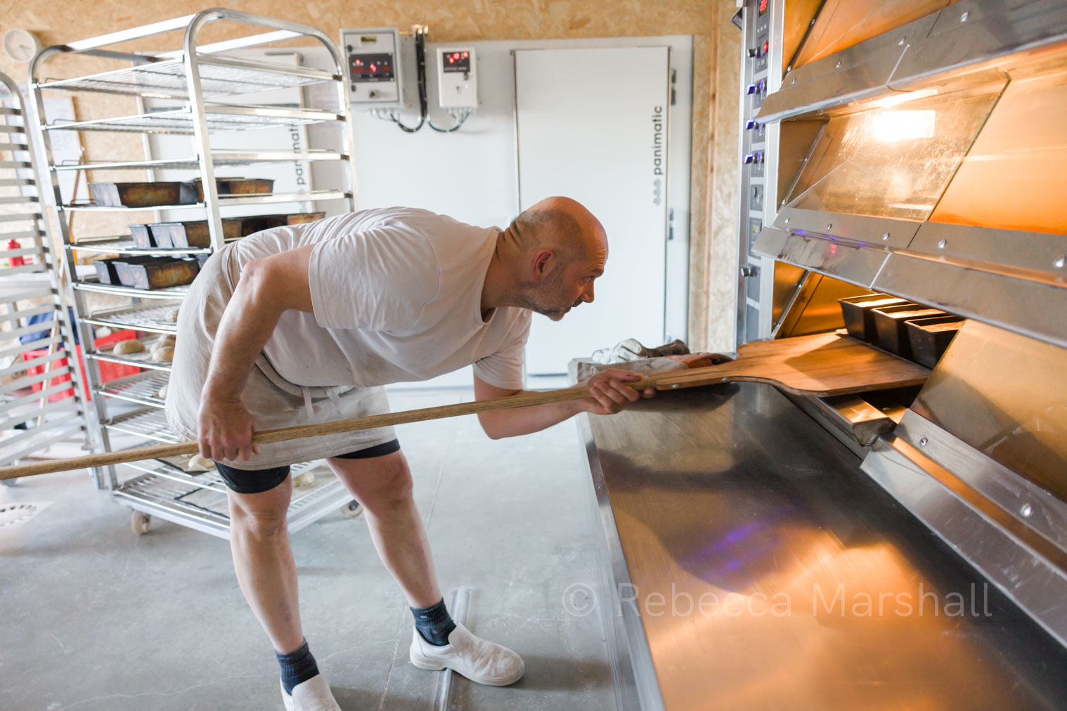 Loading the Oven with Loaves Photograph of a baker, dressed in white, putting loaves of bread into a commercial bread oven on a large wooden shovel
